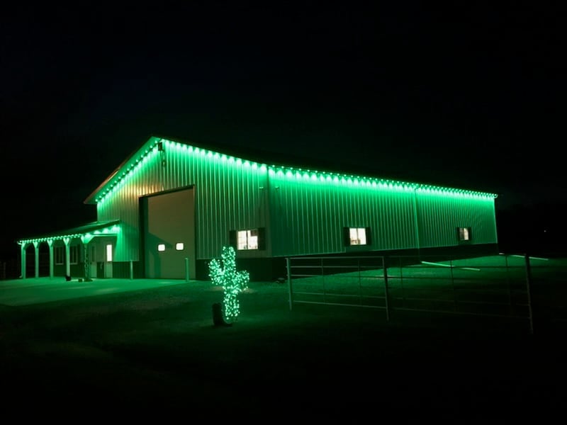 Large metal barn building illuminated with bright green neon lights at night against dark sky