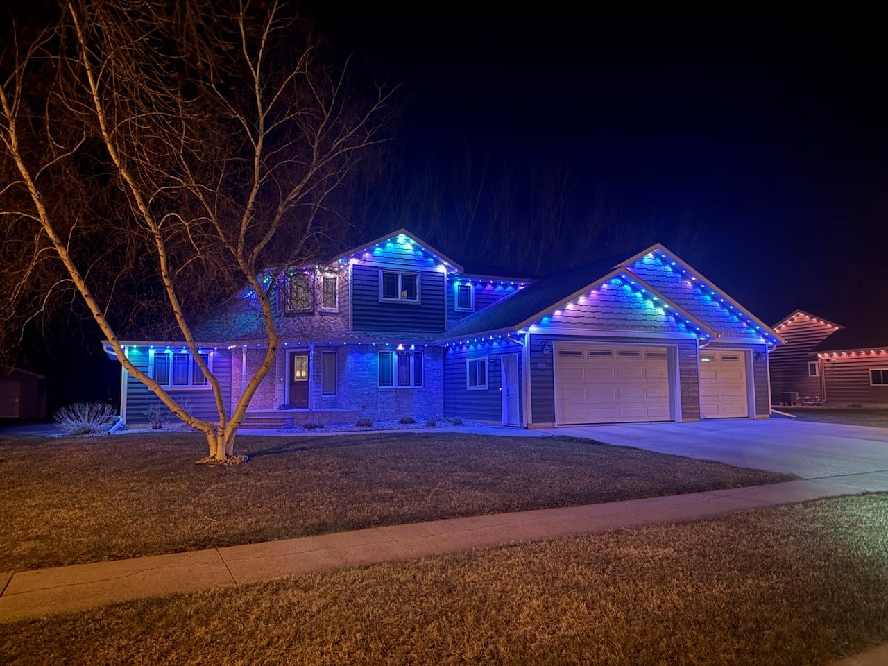 Suburban home decorated with bright blue and purple LED lights at night, featuring illuminated roofline, garage, and landscaping