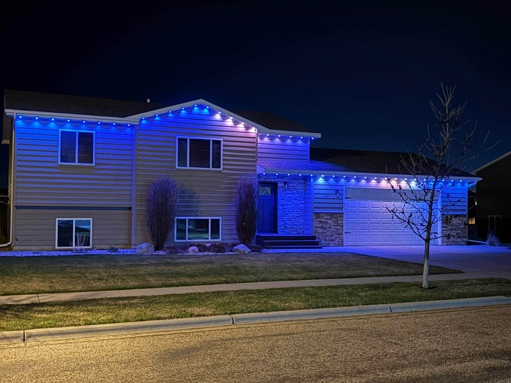 Modern two-story house with blue and purple LED lighting at night, featuring a garage and bare tree in the front yard.