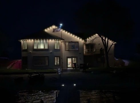 Modern house exterior lit up at night with illuminated roofline and driveway lights