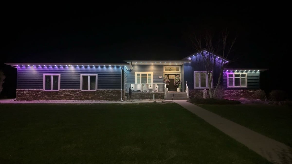 Modern single-story house illuminated at night with purple and white LED lighting, featuring a central portico and landscaped front lawn