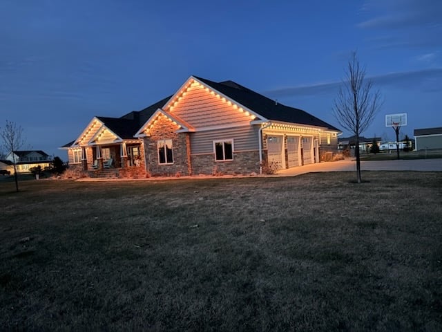Modern house with exterior lighting illuminated at dusk on expansive lawn with bare trees and fenced property