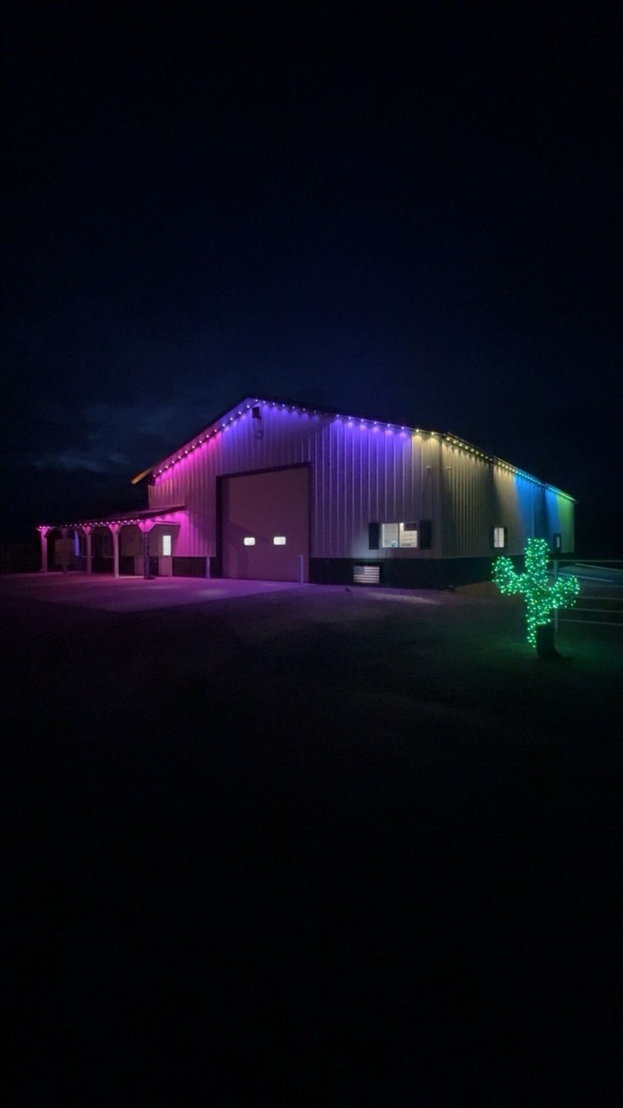 Industrial metal warehouse building illuminated with colorful neon lights in pink, purple, blue, and green at night