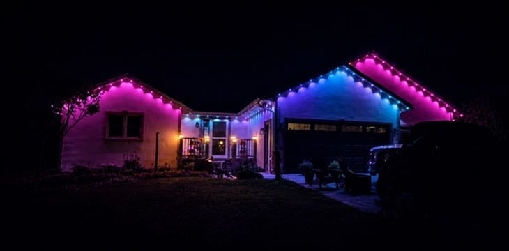 Two illuminated tiny homes at night with neon pink, blue, and purple LED lighting against a dark background